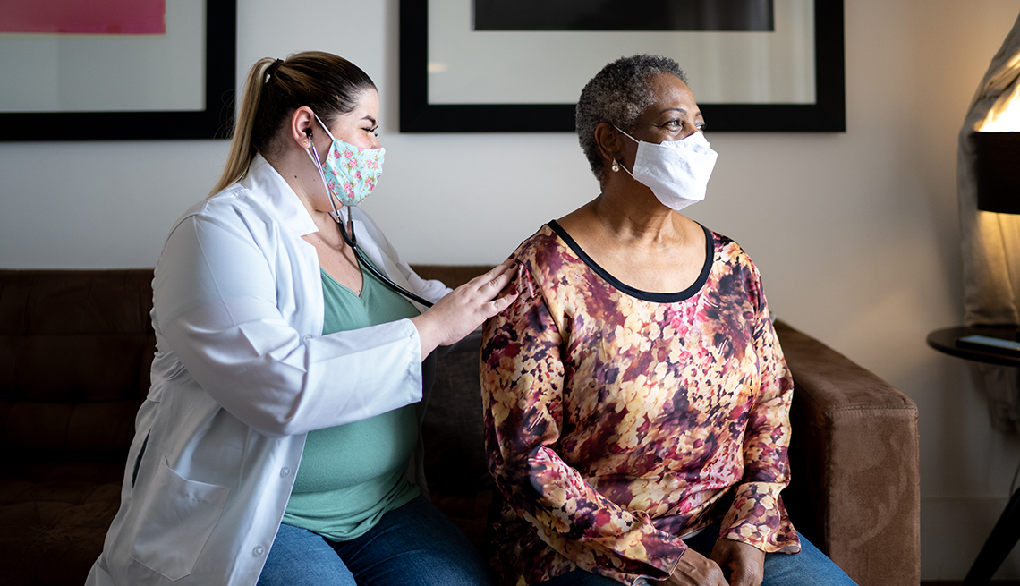 Doctor using stethoscope listening to senior patient breathing at her house - using face mask