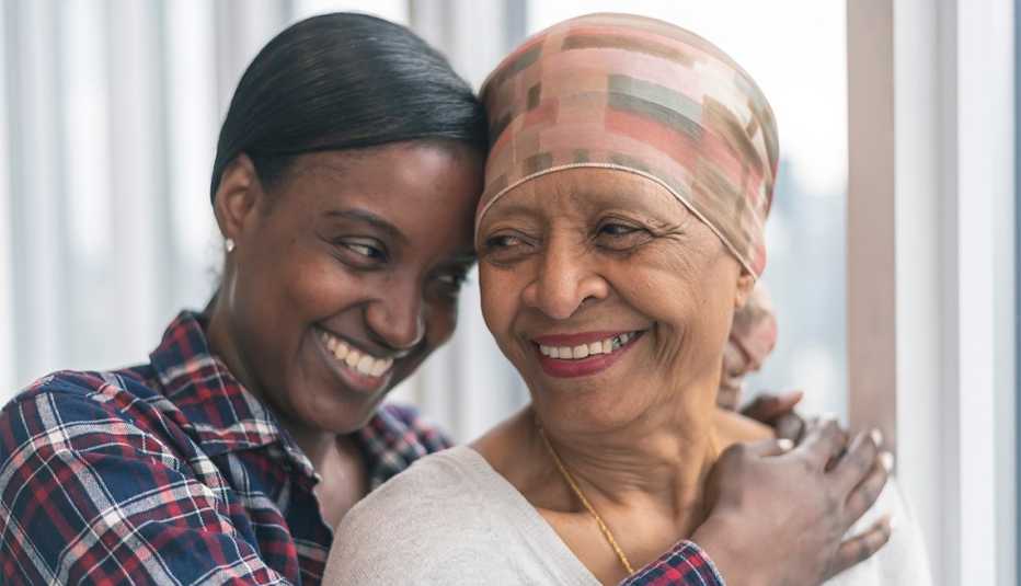 A senior woman with cancer is wearing a scarf on her head. Her adult daughter is giving her a hug. Both women are smiling with gratitude and hope for recovery.