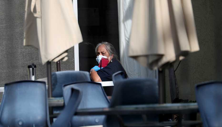 A woman sits alone at a table wearing a mask