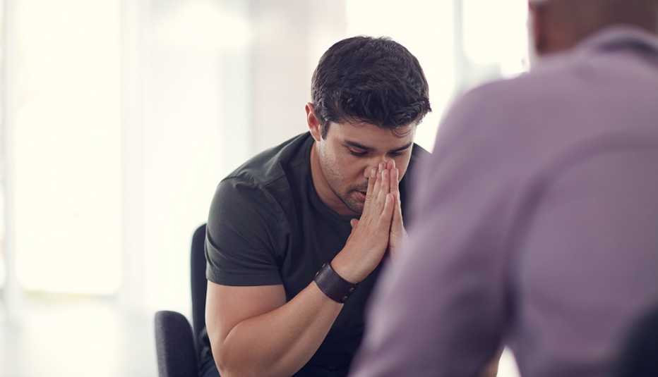 A man is sitting with his head in his hands while talking with someone