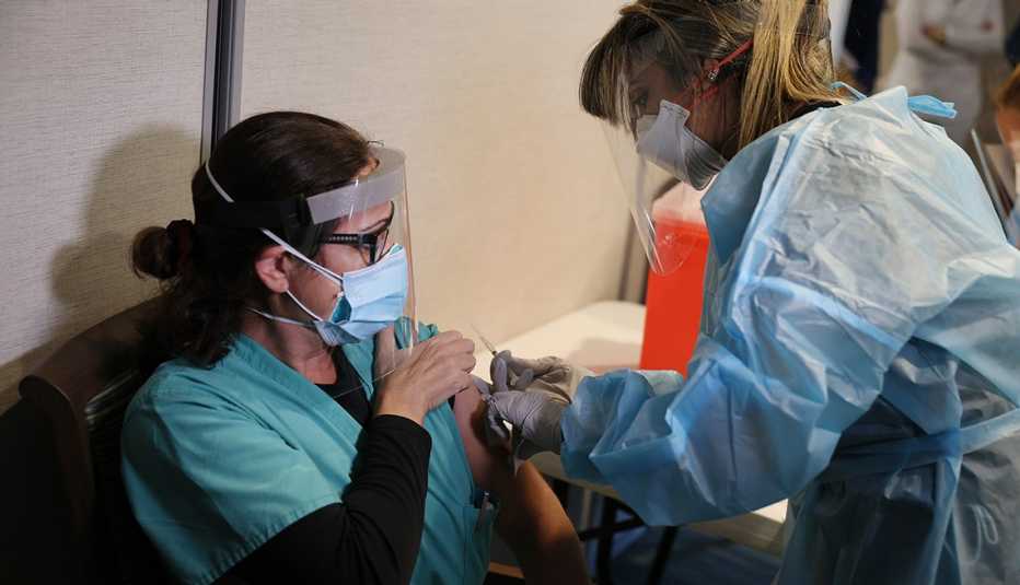 A female nursing home worker in a face mask getting a covid vaccine in the arm