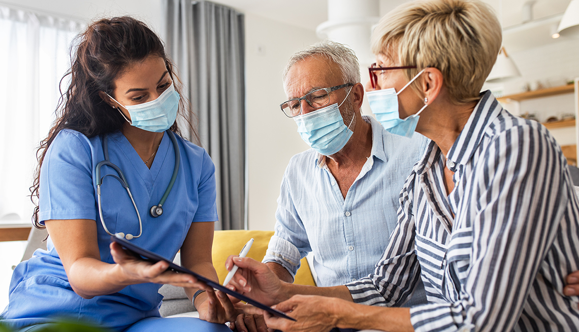 Nurse talking to a patient and caregiver and reviewing medical notes on a digital tablet.