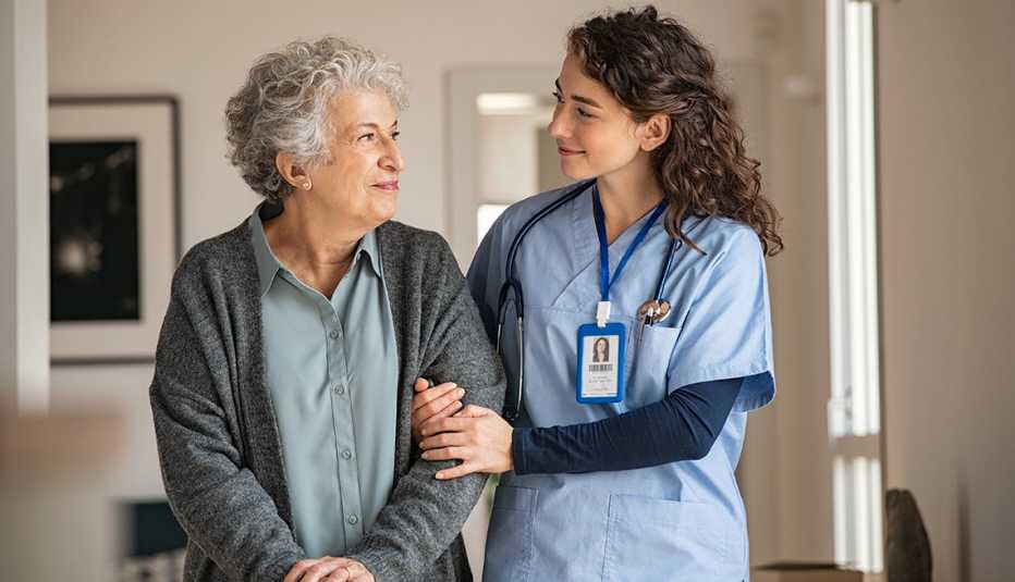 Woman with walking stick being helped by nurse at home.