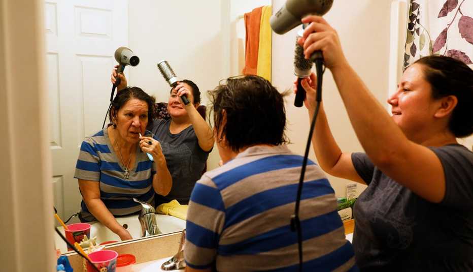 a woman brushing her teeth while her adult daughter blowdrys her hair
