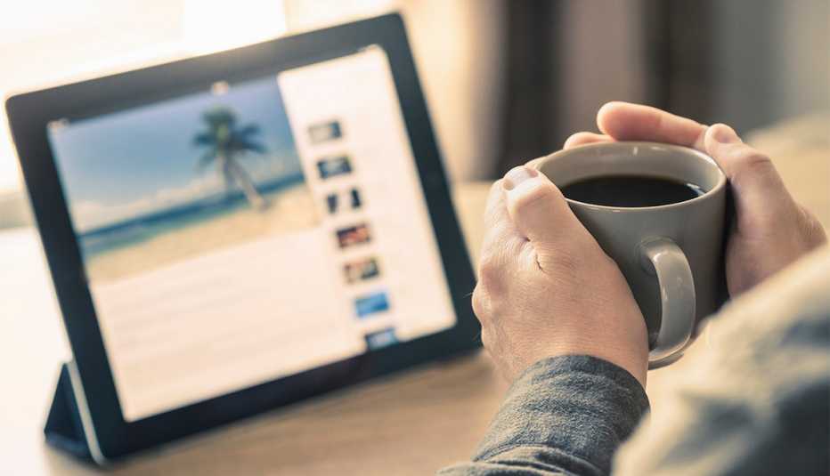 hands holding coffee with a tablet showing tropical island