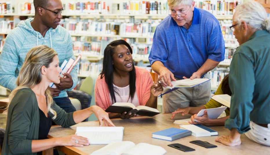 A diverse group of adult volunteers talking and comparing books in a library