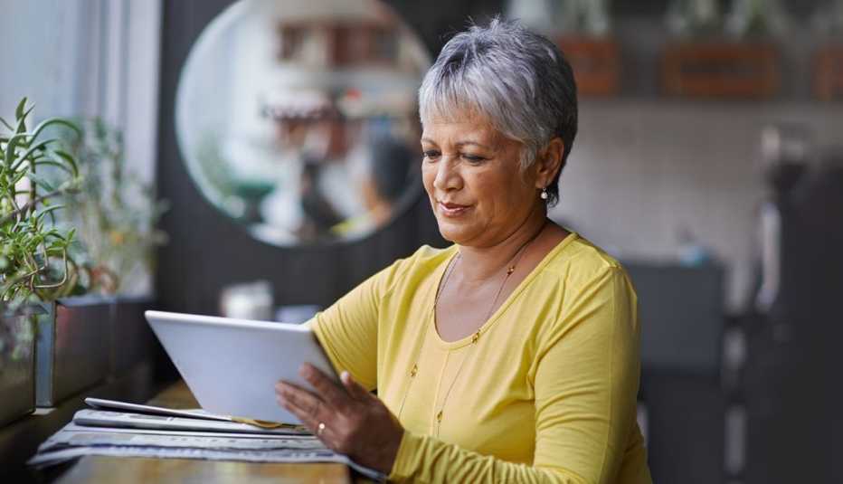 woman with short gray hair, long yellow shirt, sitting at counter, reading white tablet