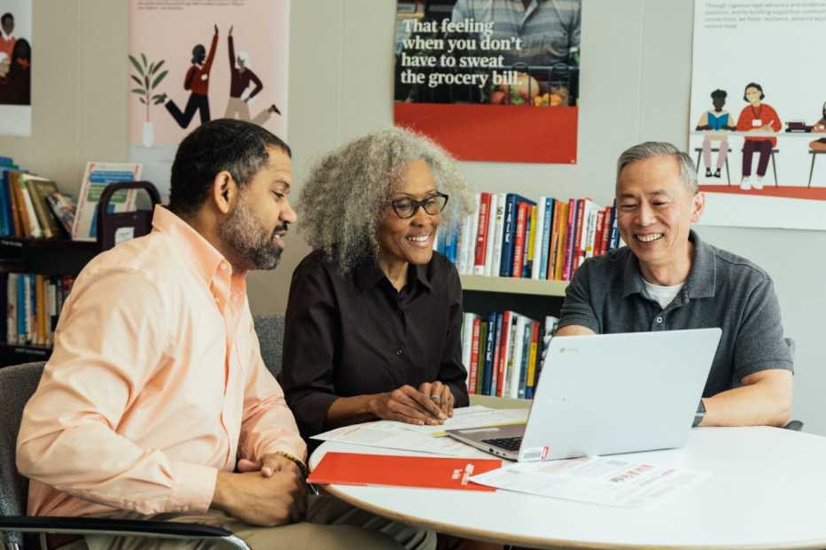 Adults gathered together around a computer smiling and surrounded by books
