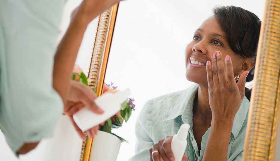 A woman applying moisturizer on her face in front of a mirror A woman applying moisturizer on her face in front of a mirror