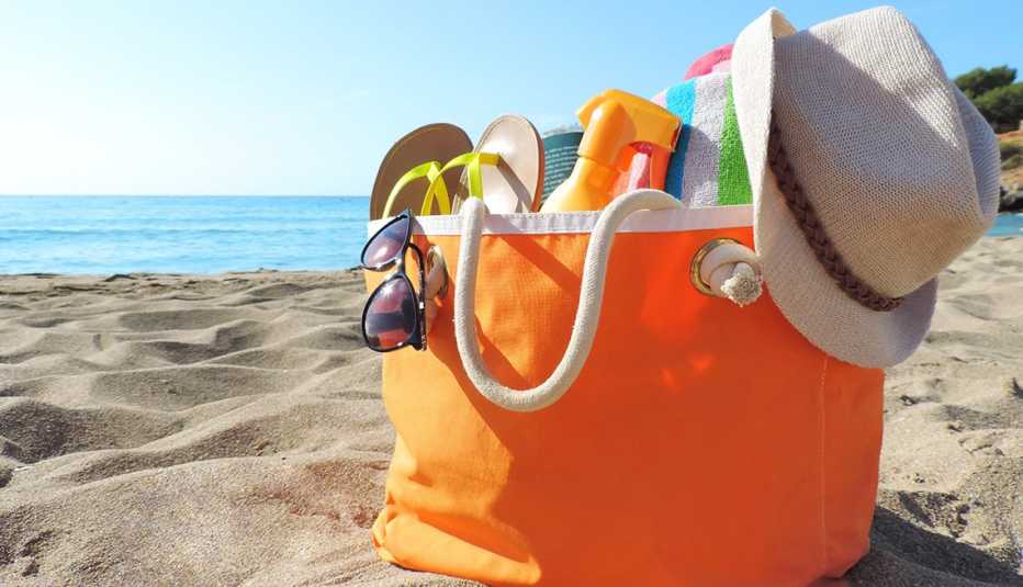 A beach bag filled with items sitting on the sand A beach bag filled with items sitting on the sand