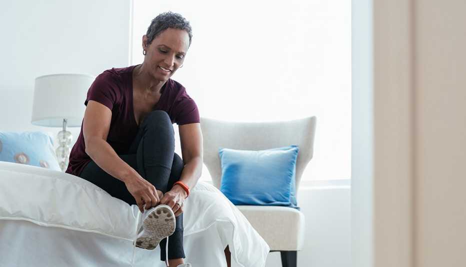 A woman putting on and adjusting sneakers in her bedroom