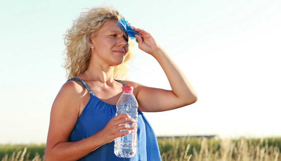 A woman wiping her forehead with a paper tissue while holding a water bottle outside A woman wiping her forehead with a paper tissue while holding a water bottle outside