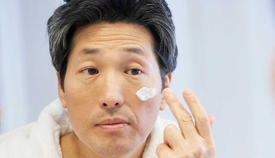 Man in front of mirror putting on eye cream.