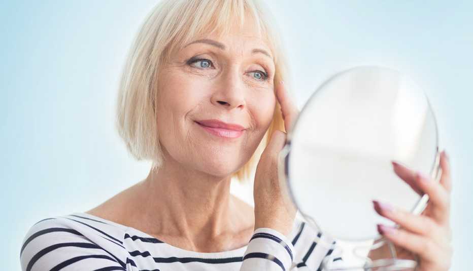 woman examines her face in a handheld mirror