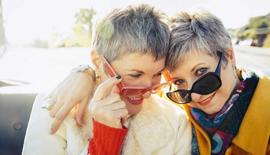 Two women wearing sunglasses while sitting in the back of a convertible.