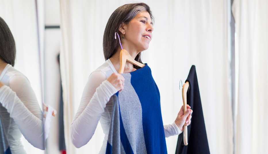 A woman examining a dress in front of her body while looking at a mirror 