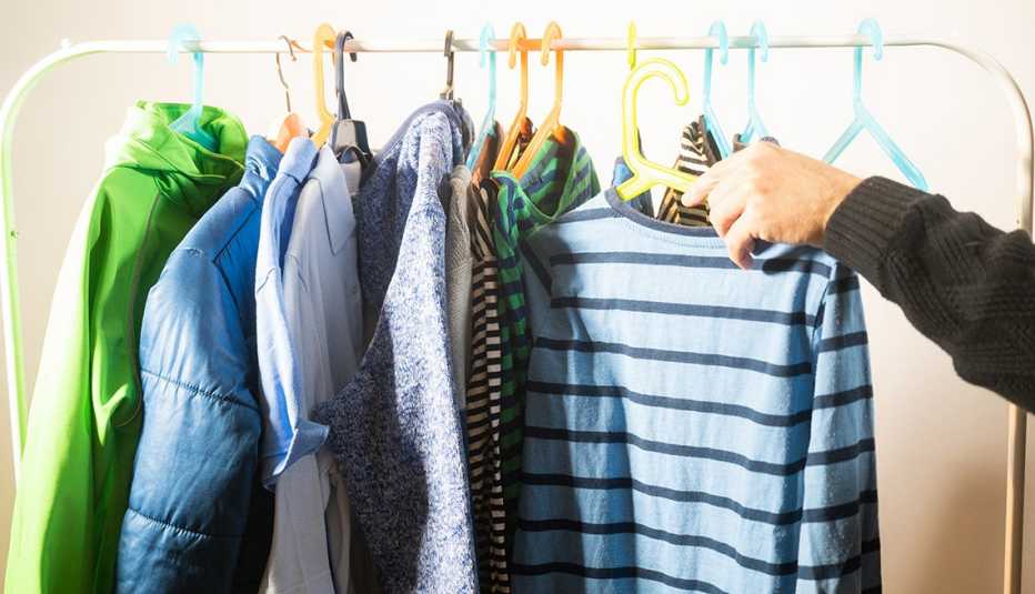 A person placing a shirt on a hanger onto a clothing rack containing other clothing