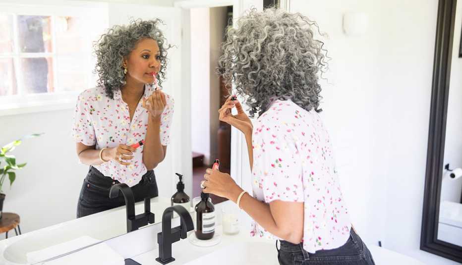 A woman applying makeup in front of a mirror in her bathroom
