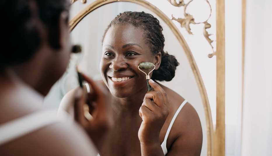 A woman using a face roller in front of a mirror