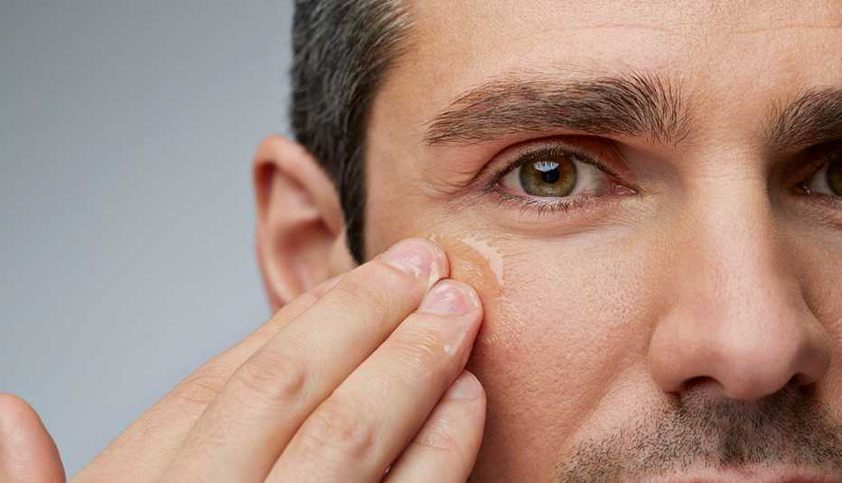 Man rubbing clear cream under his eyes.