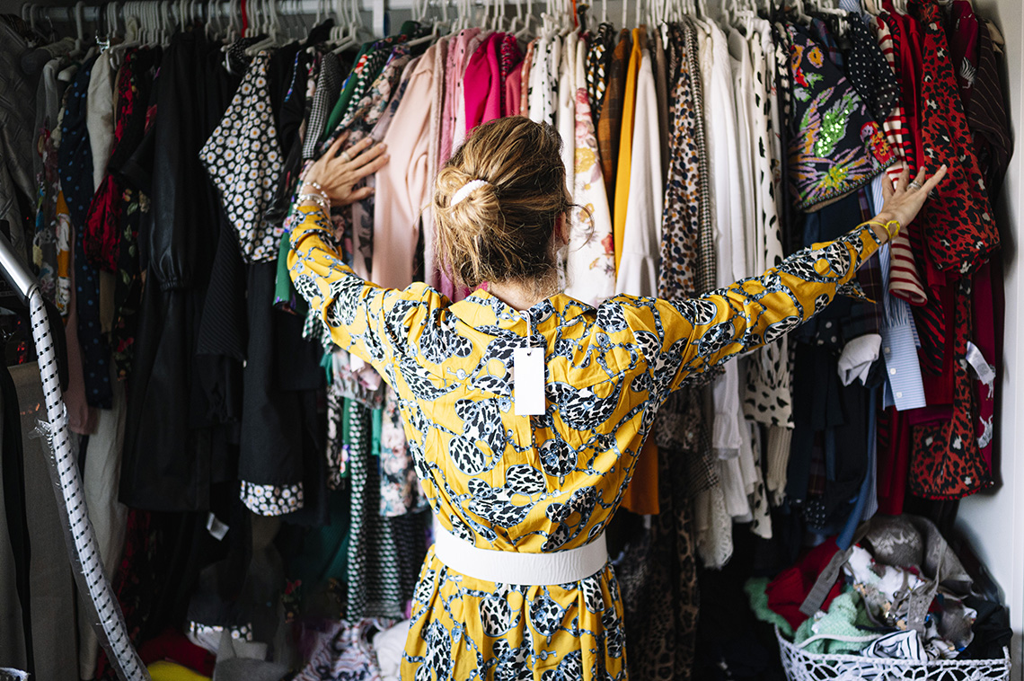 A woman in a yellow dress with its price tag looking at a closet full of clothes