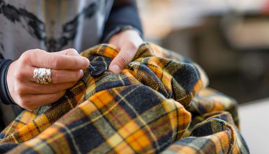 A close up of a woman hand sewing a button onto a jacket A close up of a woman hand sewing a button onto a jacket