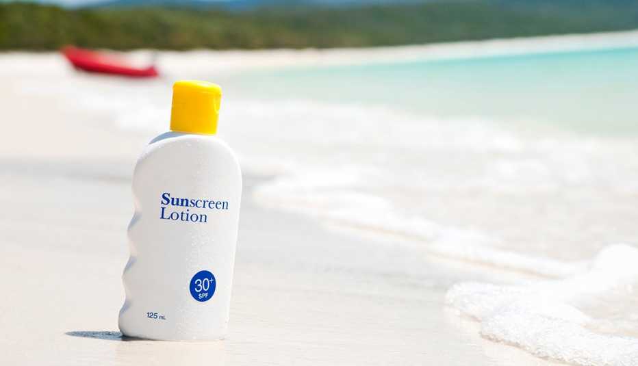 A bottle of sunscreen lotion on the sand at the beach nearby the ocean