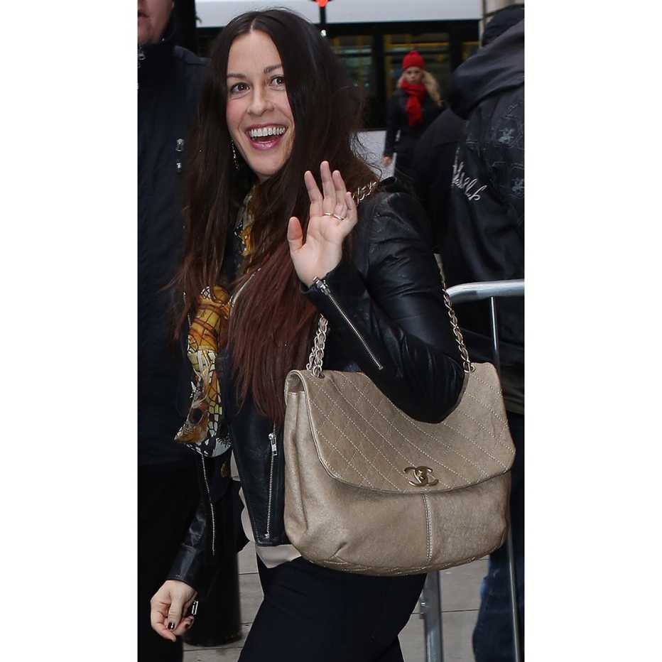 Alanis Morissette tucks a flap shoulder bag with chain strap under her arm.