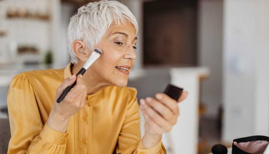A woman in a yellow blouse applying makeup on her face with a brush A woman in a yellow blouse applying makeup on her face with a brush