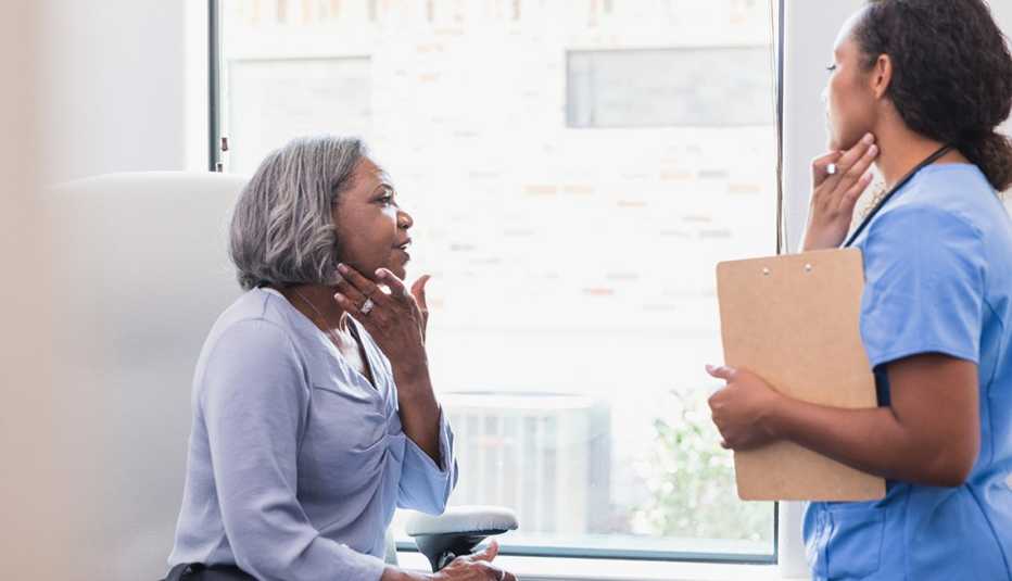 A woman gestures towards her face while talking with a dermatologist