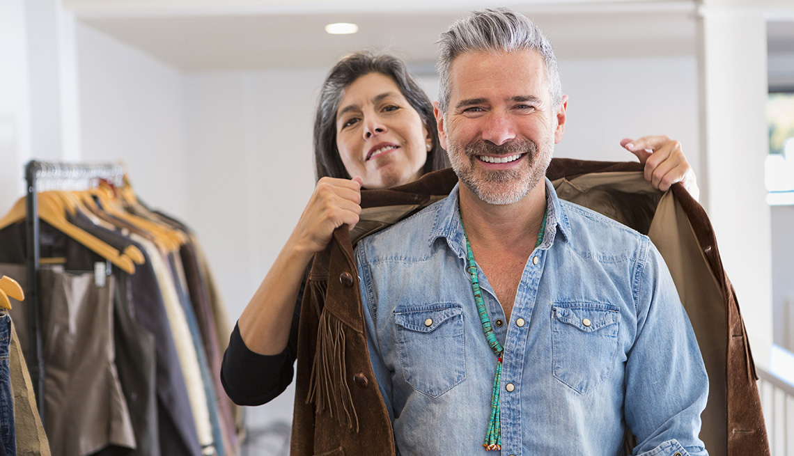 A woman helping a man put on a brown jacket in a store