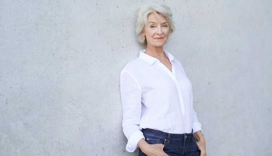 A woman wearing a white button-down shirt leaning against a concrete wall