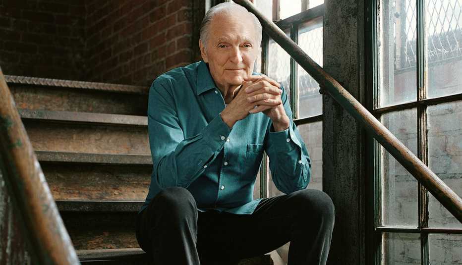 alan alda sits on a metal staircase