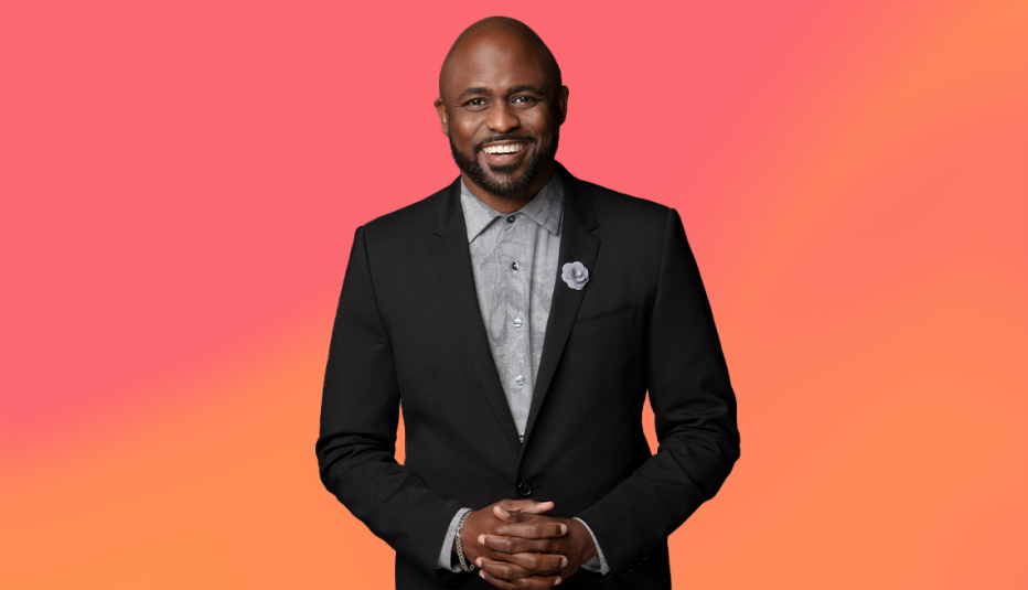 wayne brady in black business suit against pinkish orange ombre background
