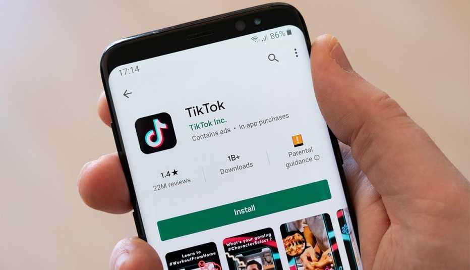 A man's hand holding a smartphone displaying the Google Play install screen for the video sharing social media app Tik Tok