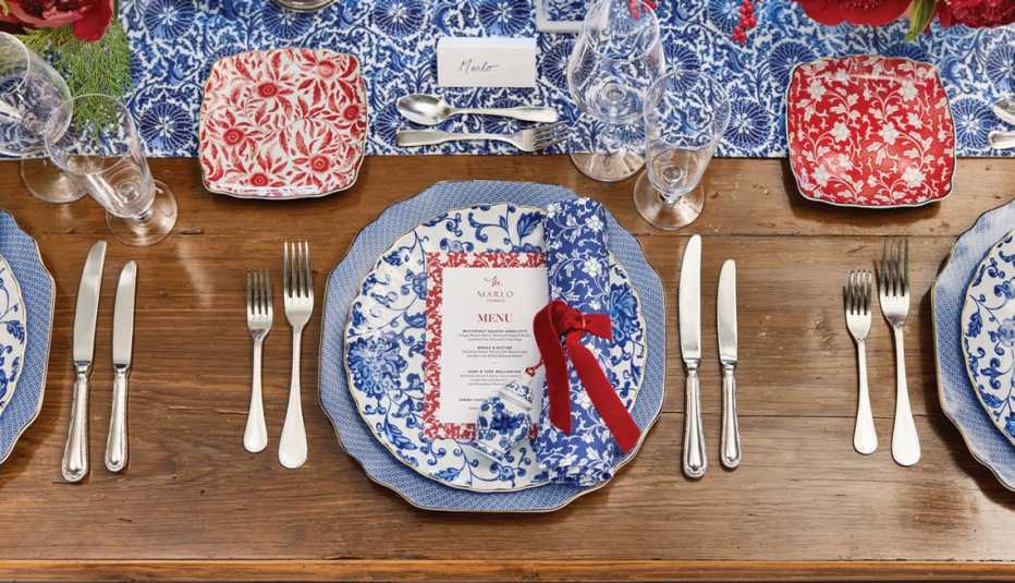 plate with menu on it, knives on right, forks on left, glasses on upper right, small plate on upper left