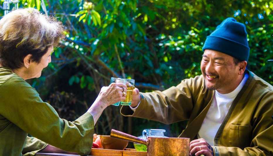 Roy Choi sitting at an outdoor table clinking glasses with Alice Waters, whose back is to the camera