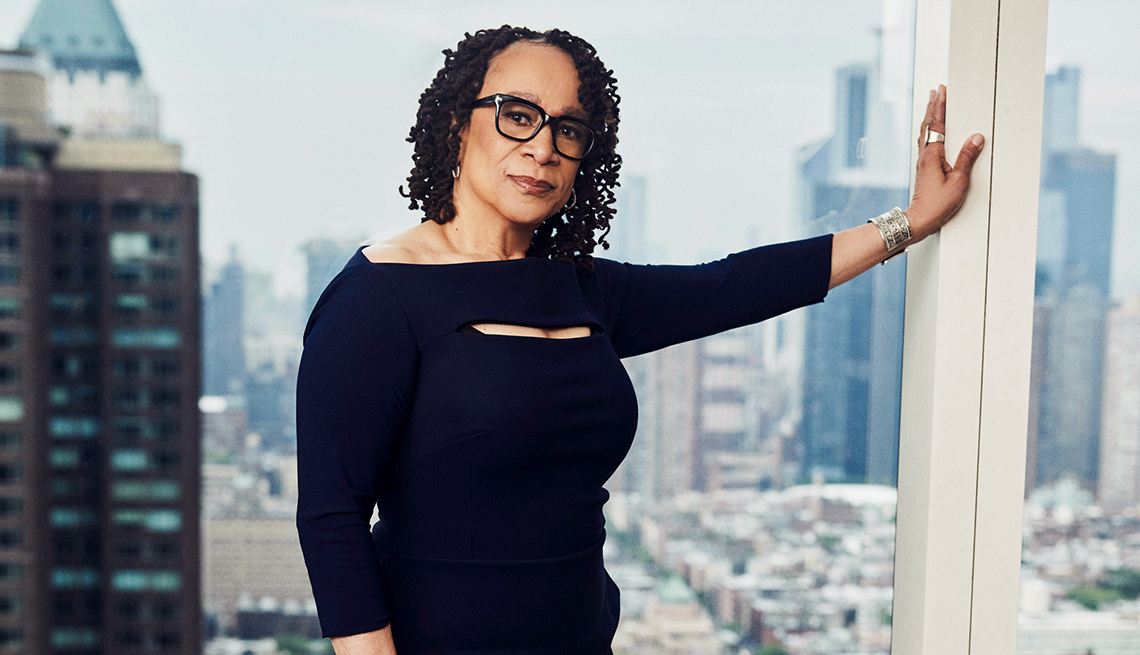 S. Epatha Merkerson in a black dress leaning against a window overlooking city buildings