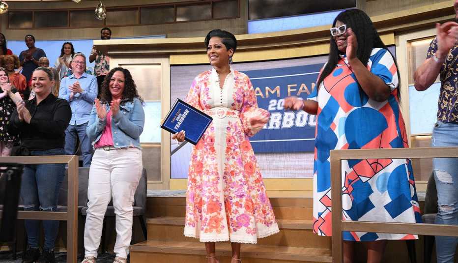 Tamron Hall pictured with audience members of her show tamron hall on steps on the set of her show with audience members on both sides of her