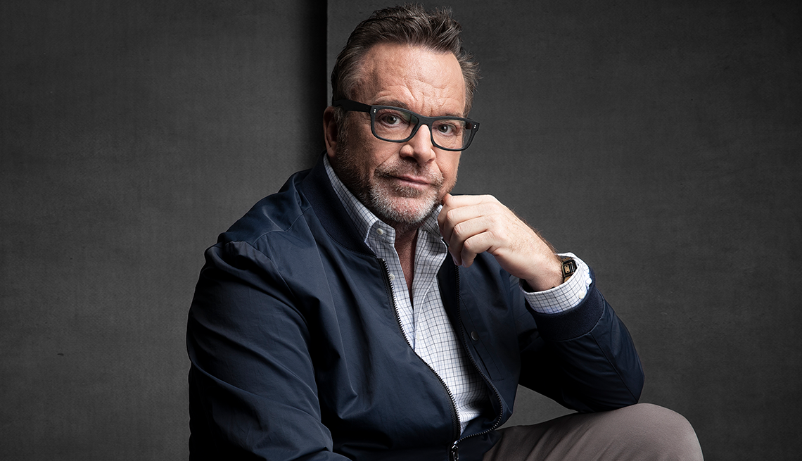 tom arnold resting cheek against left hand; dark gray background