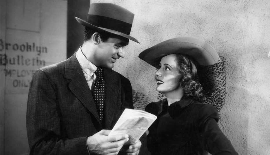 Cary Grant holds a folded newspaper and looks at Irene Dunne while they stand outside the employee's entrance of the Brooklyn Bulletin in the film "Penny Serenade."