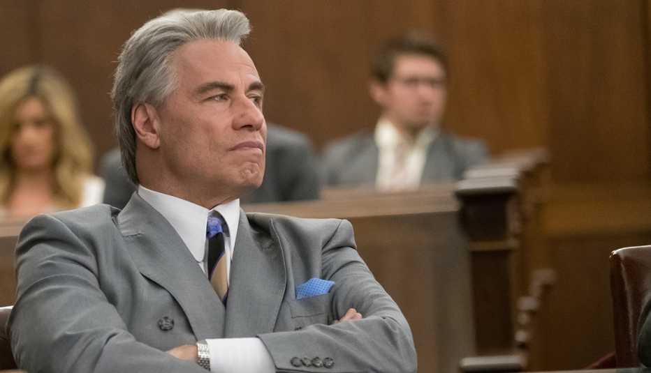 John Travolta sitting at a table with arms crossed. John Travolta sitting at a table with arms crossed.