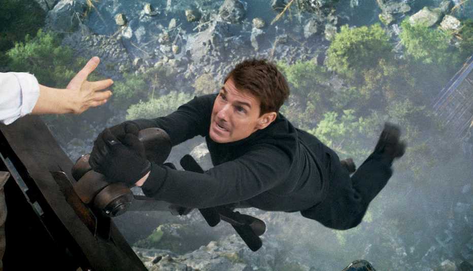 Tom Cruise stars as Ethan Hunt in the film, "Mission: Impossible - Dead Reckoning Part One." tom cruise hanging from the end of a train car high in the air in the film mission impossible dead reckoning part one