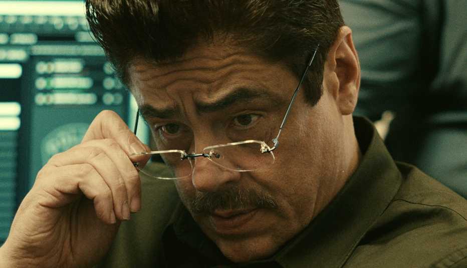 Benicio Del Toro stars as Tom Nichols in "Reptile." benicio del toro pulls down his glasses in a scene from the netflix film reptile