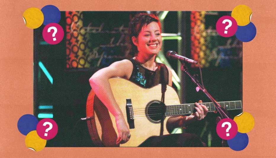 Sarah McLachlan holding guitar, standing behind microphone; surrounded by blue, yellow and pink circles with question marks in them