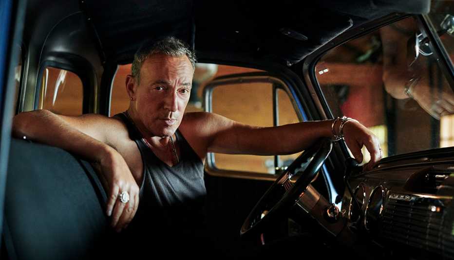 bruce springsteen poses in the drivers seat of one of his antique cars