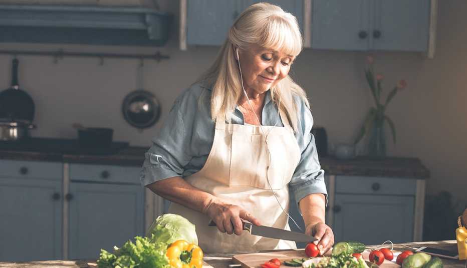 A woman cutting vegetables in the kitchen while wearing headphones A woman cutting vegetables in the kitchen while wearing headphones