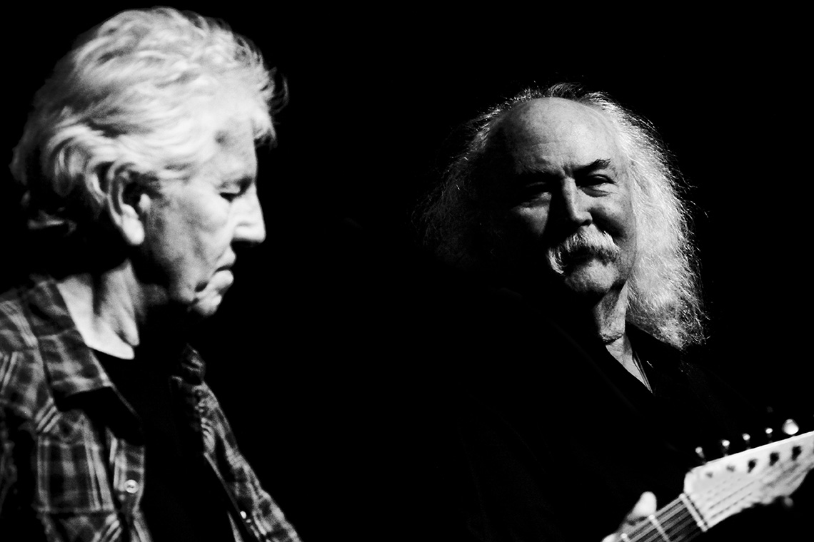 Graham Nash playing the guitar next to David Crosby