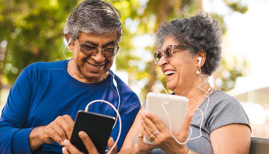smiling couple seated in a park plugged into mobile devices