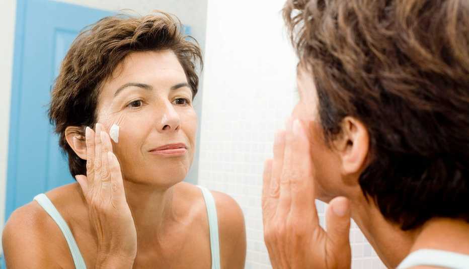 woman applying eye cream in mirror